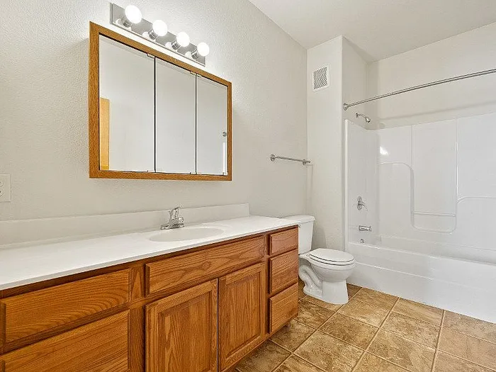Bright and spacious bathroom featuring a sleek vanity with wooden cabinets, large mirror, and a pristine bathtub with modern fixtures.