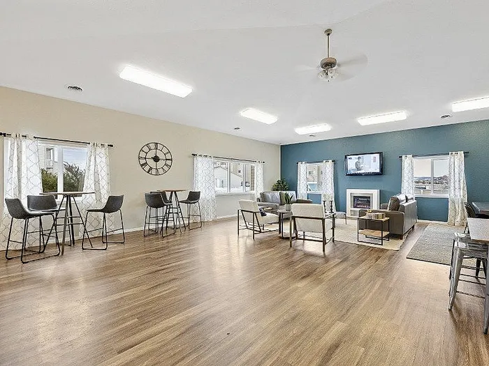 Bright, spacious community room with modern decor, hardwood floors, comfortable seating, and natural light from large windows.