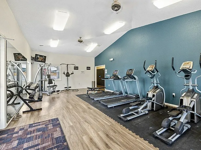 Modern fitness center with state-of-the-art treadmills, elliptical machines, and weight equipment on a stylish wood floor and vibrant blue wall.
