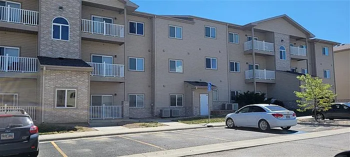 Modern apartment building with balconies, ample parking, and a welcoming facade under a clear blue sky.