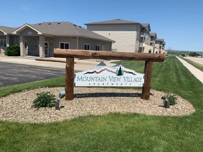 Charming Mountain View Village Apartments entrance sign, surrounded by green lawns and modern buildings under clear blue skies.