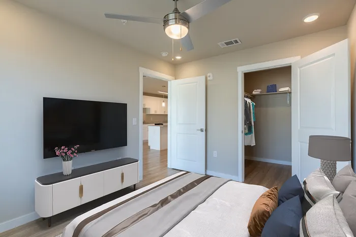 Cozy bedroom with stylish decor, flat-screen TV, and open walk-in closet, leading into a modern kitchen.