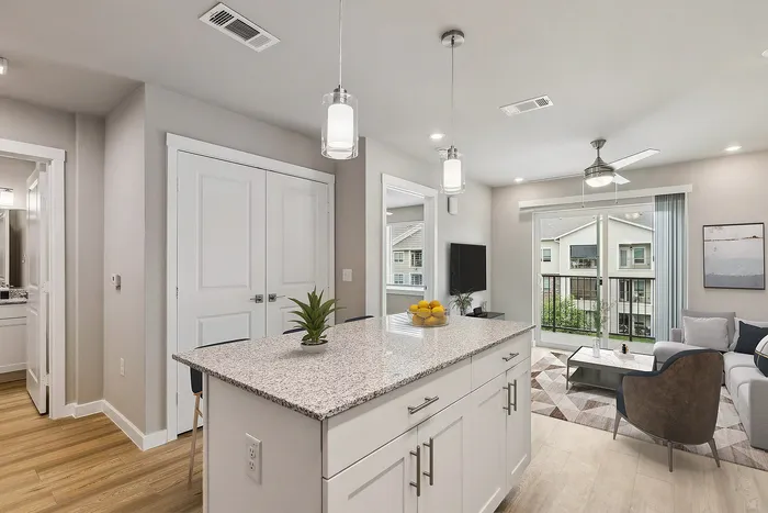 Chic apartment interior showcasing a sleek kitchen island, open living area, and bright sliding glass doors leading to a balcony.