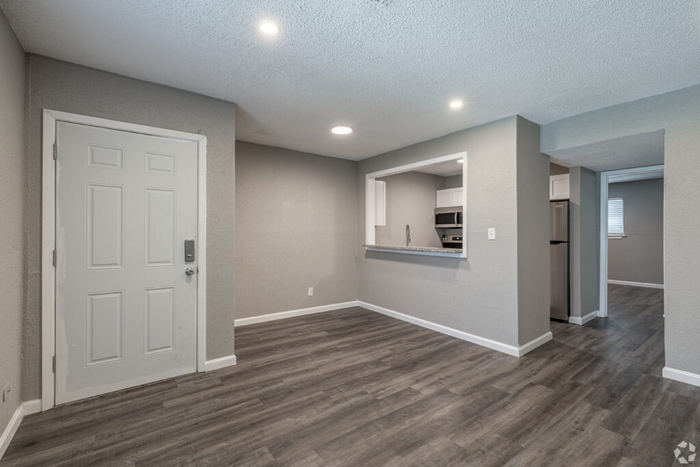 Modern open-concept living space with sleek grey flooring, contemporary kitchen pass-through, and recessed lighting.