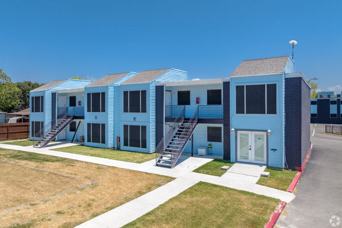 Charming apartment complex with vibrant blue siding, featuring modern double-story units and well-maintained lawns under a clear sky.
