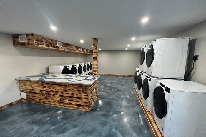 Modern laundry room with sleek machines, polished concrete floors, and unique wood accents.