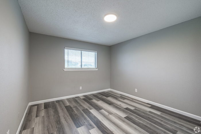 Bright and spacious bedroom with modern gray wood flooring and a large window for natural light.