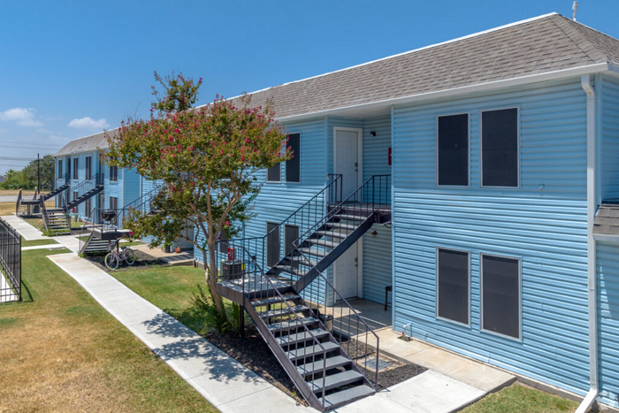 Charming blue apartment building with outdoor stairs and lush greenery, offering a serene living environment.