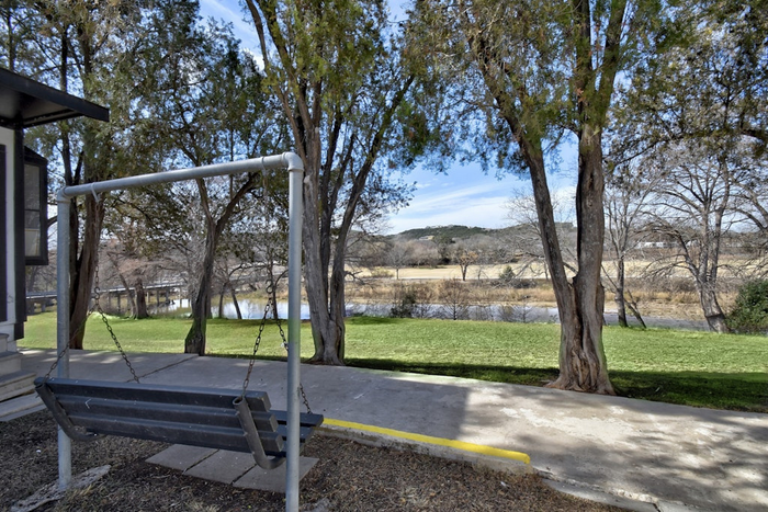 Serene apartment view featuring a charming backyard swing under tall trees overlooking a tranquil river and scenic countryside.