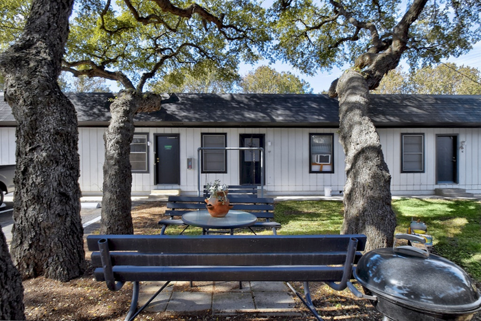 Charming outdoor space with shaded picnic benches, surrounded by mature trees, enhancing the rustic appeal of a cozy cottage-style apartment.