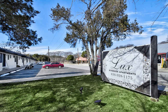 Lux Riverside Apartments sign in a scenic setting with lush green grass and ample parking, promising comfortable living.