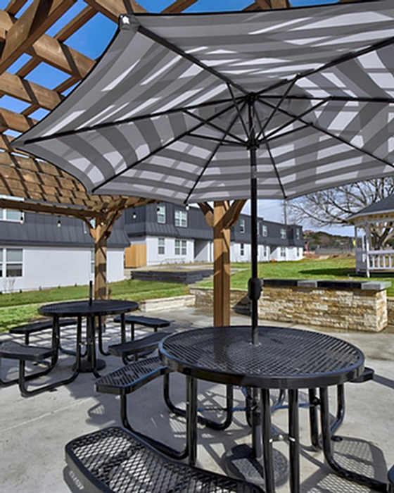 Charming outdoor space with elegant picnic tables under a stylish pergola and striped umbrellas, perfect for relaxation and social gatherings.