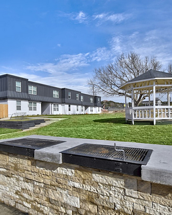 Charming apartment exterior with modern architecture, lush green lawn, and a cute gazebo perfect for outdoor gatherings.