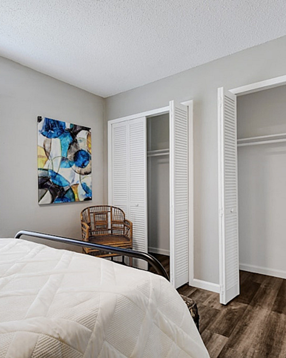 Cozy bedroom with modern decor, featuring a comfortable bed, open closets, artistic wall art, and warm wood flooring.