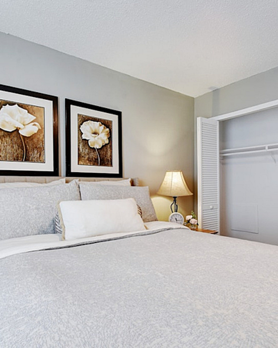 Inviting bedroom with serene decor, featuring a cozy bed with plush pillows, elegant floral artwork, and a spacious closet.