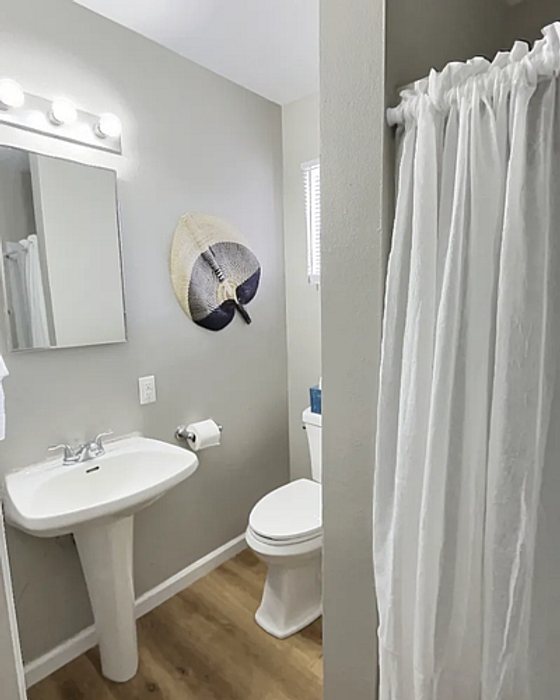 Modern bathroom with sleek pedestal sink, stylish wall decor, and bright lighting, featuring elegant wood flooring and a cozy shower area.