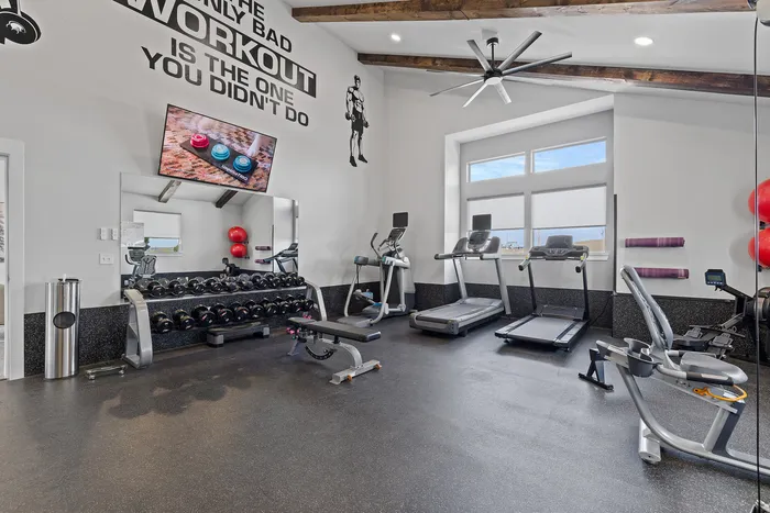 Modern fitness center featuring top-of-the-line treadmills, exercise bikes, and a comprehensive weight set under stylish exposed beams.