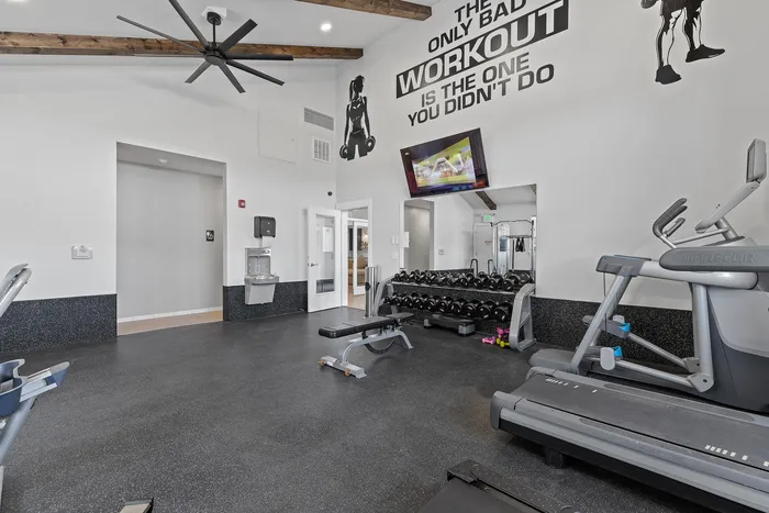 Modern fitness center with state-of-the-art equipment, including treadmills and weights, under stylish ceiling beams.