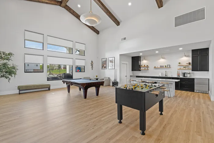 Luxurious open-concept game room featuring a pool table, foosball, and sleek modern kitchen with high ceilings and abundant natural light.