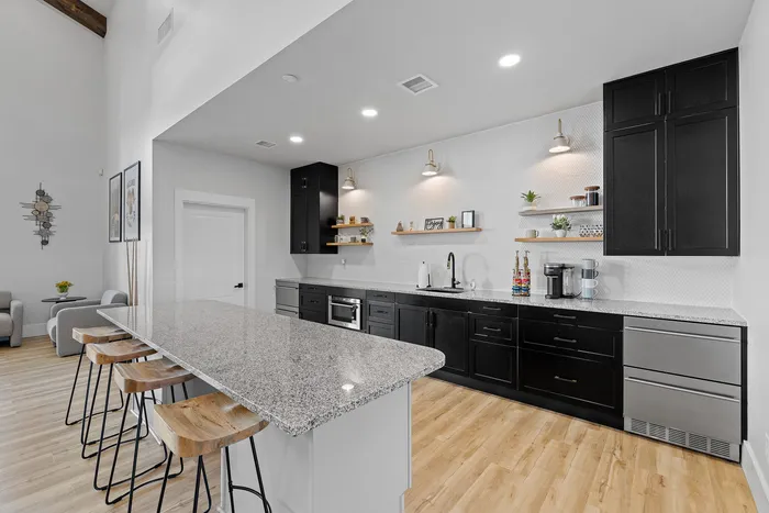 Modern kitchen with sleek black cabinets, open shelving, and a spacious granite countertop island, perfect for entertaining in a stylish open-concept layout.