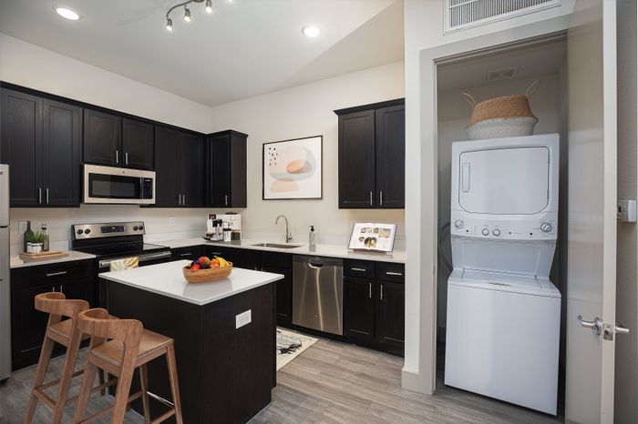 Modern kitchen with sleek dark cabinetry, stainless steel appliances, and a cozy island bar in an elegant apartment setting.