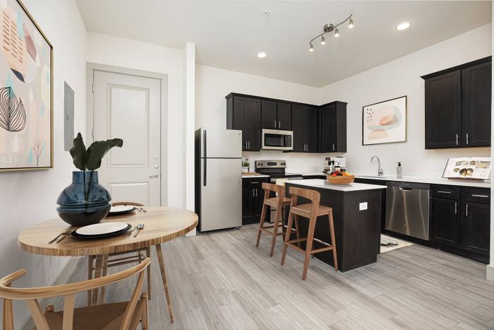 Modern kitchen with sleek black cabinetry, stainless steel appliances, and a chic island bar complete with wooden stools; dining area features an elegant circular table with stylish decor.