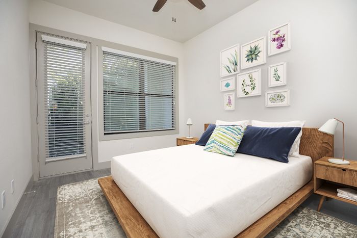 Inviting bedroom with modern decor featuring a comfortable bed, artistic floral wall art, and ample natural light from large windows.
