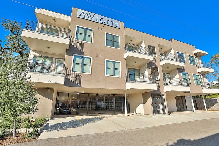 Modern apartment complex with sleek balconies, ample windows, and garage parking, set against a vibrant blue sky.