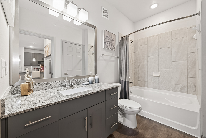 Modern bathroom with sleek granite countertops, elegant cabinetry, and a stylish tiled bathtub-shower combo.