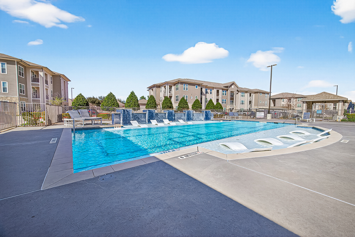 Inviting apartment complex showcasing a luxurious pool area with modern lounge chairs, perfect for relaxation under a clear blue sky.