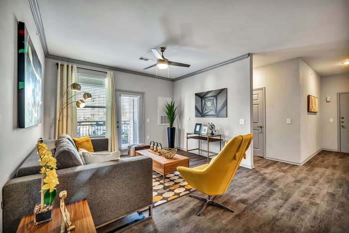 Modern living room with elegant decor, featuring a cozy gray sofa, vibrant yellow accents, stylish artwork, and large windows for natural light.
