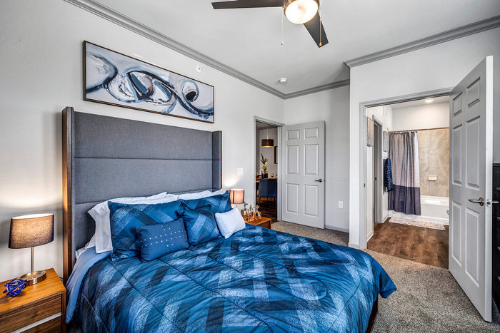 Modern bedroom with plush queen bed, stylish artwork, and en-suite bathroom entrance, bathed in natural light with elegant furnishings.