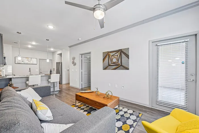 Bright and modern living room featuring a sleek gray sofa, stylish wooden coffee table, and vibrant yellow accent chair. Open-concept design with a chic kitchen island and contemporary decor.