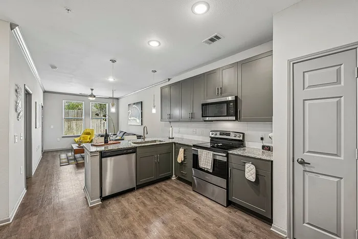 Modern apartment kitchen with sleek gray cabinets, stainless steel appliances, and an inviting open layout leading to a cozy living area with stylish decor.