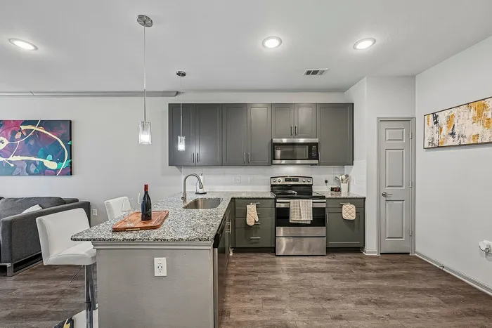 Modern open-concept kitchen with sleek gray cabinets, granite countertops, and stylish pendant lighting, adjacent to a cozy living area with contemporary decor.