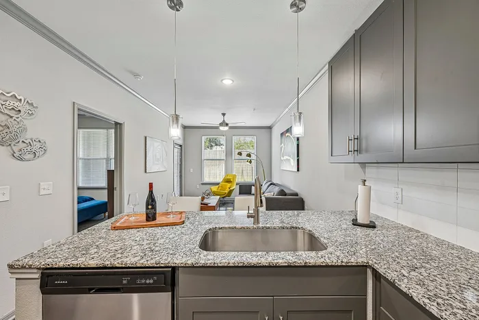 Modern open-plan apartment featuring a sleek granite kitchen island, elegant pendant lighting, and inviting living area with a vibrant yellow chair.