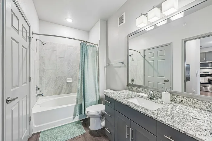 Modern bathroom featuring a granite countertop vanity, stylish tile shower, and elegant lighting fixtures.