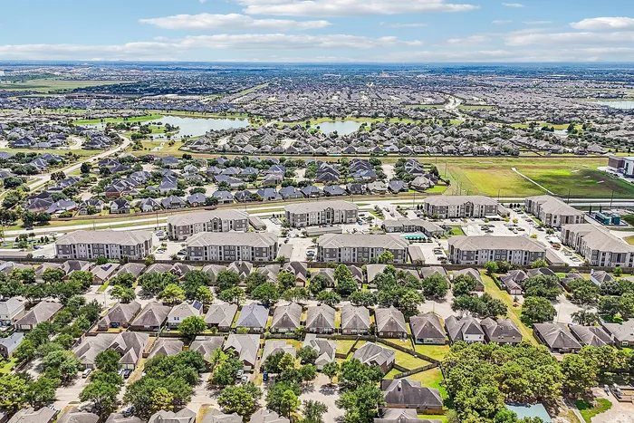 Breathtaking aerial view of a vibrant suburban community featuring modern apartment complexes, lush greenery, and tranquil water bodies under a bright sky.