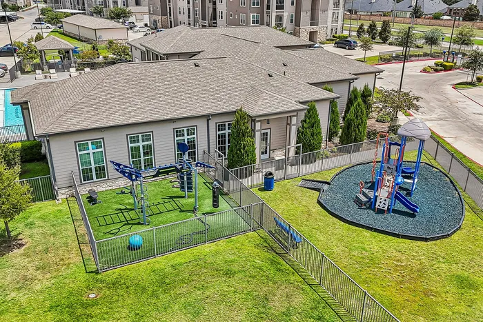 Modern apartment complex with vibrant outdoor amenities featuring a playground and fitness area surrounded by lush greenery.