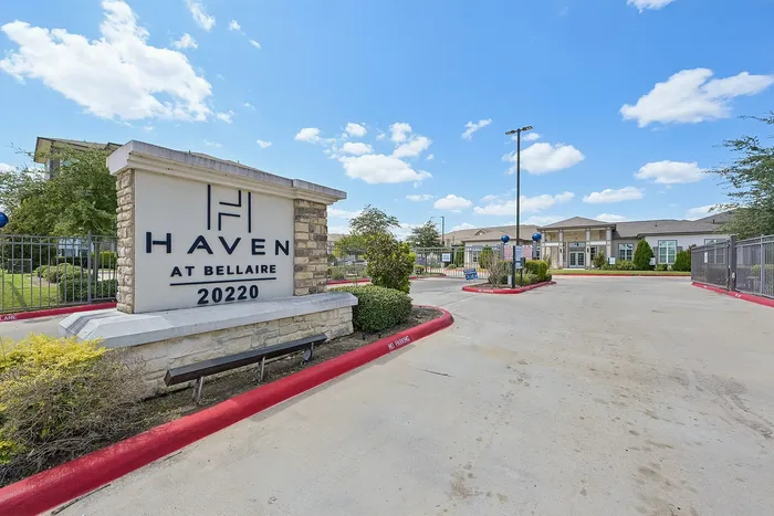 Welcoming entrance to Haven at Bellaire with vibrant greenery and modern architecture under a bright blue sky.