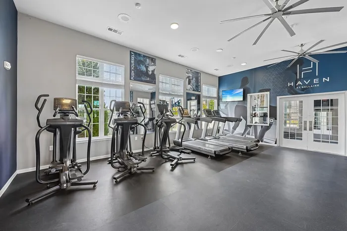 Modern fitness center featuring state-of-the-art treadmills and elliptical machines, set in a bright, spacious room with motivational decor and large windows.