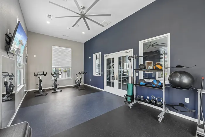 Contemporary fitness room featuring exercise bikes, a sleek ceiling fan, and well-organized gym equipment for an invigorating workout experience.