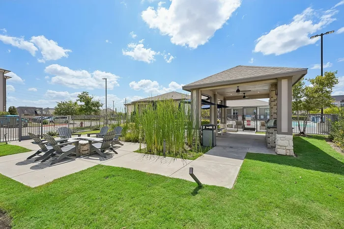 Charming outdoor patio area with stylish seating, lush greenery, and a spacious gazebo under a bright blue sky.
