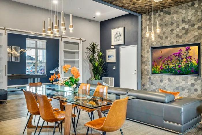 Modern living area with a sleek glass dining table, stylish leather chairs, and ambient lighting; vibrant wall art and lush indoor plants enhance the elegant decor.