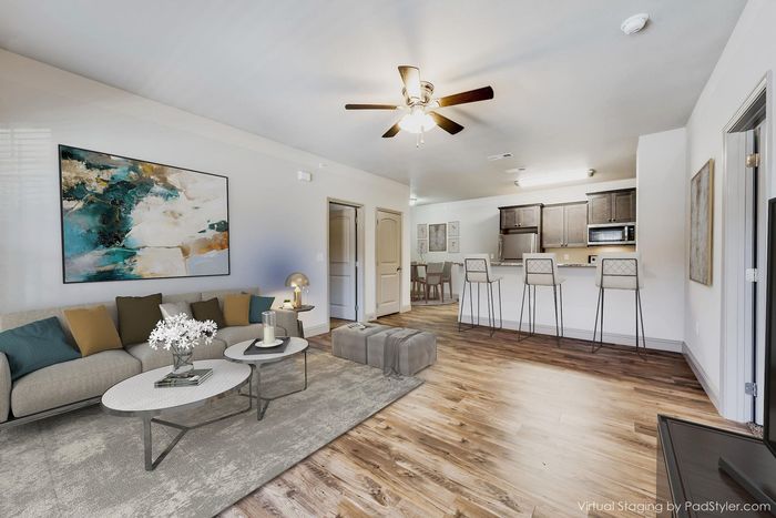 Modern open-concept living room featuring elegant hardwood floors, cozy seating area, stylish artwork, and a sleek kitchen with bar seating.
