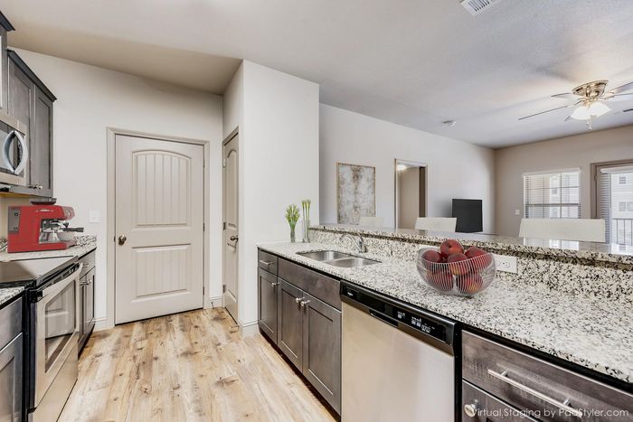 Modern kitchen with granite countertops, stainless steel appliances, and a cozy open layout, accented by a stylish red coffee machine and natural wood flooring.