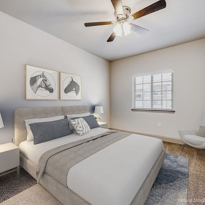 Inviting bedroom with plush carpeting, modern artwork, and a cozy bed, enhanced by ample natural light from a large window and a stylish ceiling fan.