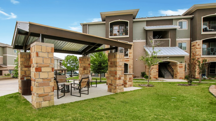 Charming apartment complex with a stylish outdoor seating area under a stone gazebo, surrounded by lush greenery.
