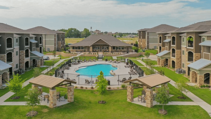 Elegant apartment complex with landscaped gardens, modern amenities, and a sparkling central pool surrounded by stylish outdoor seating.