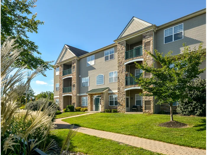 Plymouth Meeting, PA Apartments - Plymouth Pointe - View of Building Exterior with Stone Details, Neutral Tones Surrounded by Lawn, Trees, and Walking Path